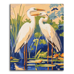 A bold, graphic paint by numbers scene of two white egrets standing side by side in shallow blue water, with reeds, green lily pads, and orange water lilies reflected around their long legs.