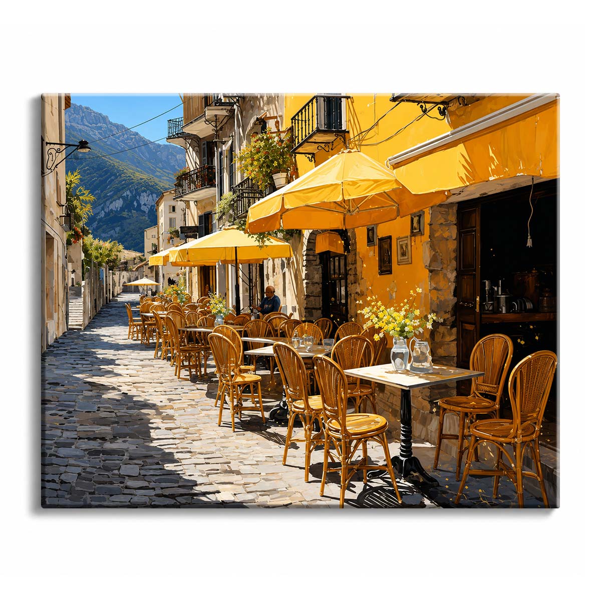 A cobbled street lined with bentwood chairs, tables and yellow umbrellas runs past a café toward a green mountain in the distance.